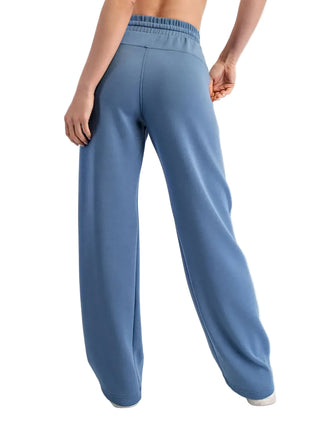 A person shown from the back wearing wide-leg blue sweatpants with an elastic waistband, photographed against a plain light gray studio background.