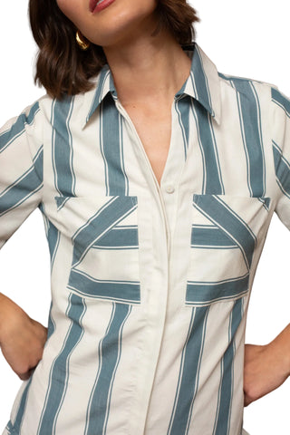 A close-up of a woman wearing a short-sleeve button-up shirt with vertical blue stripes on an off-white base, featuring diagonal striped chest pockets.