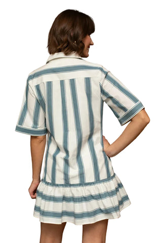 A woman wearing a short-sleeve collared shirt dress with vertical blue and white stripes, shown from the back in an indoor setting with a wooden slatted wall.
