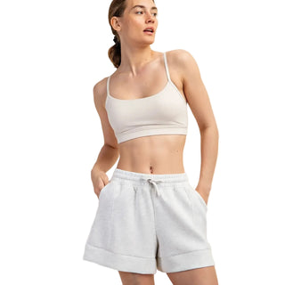 Woman wearing a white sports bra and light gray sweat shorts on a beige background