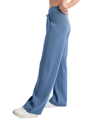 A person wearing wide-leg blue sweatpants and white sneakers, shown from the waist down against a plain light gray studio background.