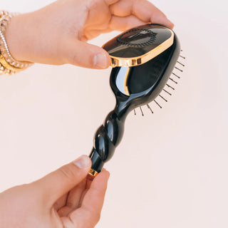 Black hairbrush with gold accents held by a hand against a light background