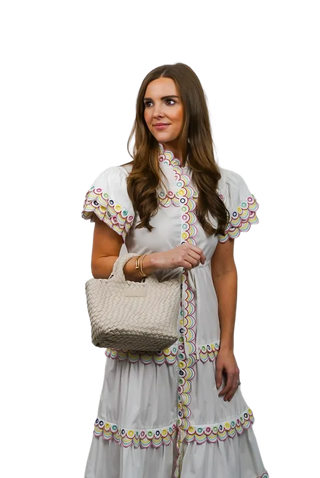 Woman wearing a white dress with colorful embroidery, holding a woven bag on a white background