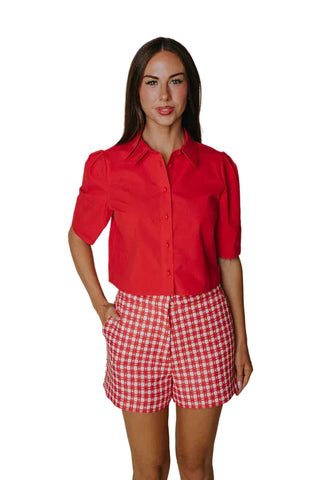 Woman wearing a red shirt and red and white checkered shorts against a plain background