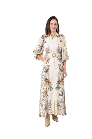 A woman modeling a long-sleeved cream-colored maxi shirt dress with a brown and beige botanical pattern, featuring a matching belt with a round gold-tone buckle, set against a plain white studio background.