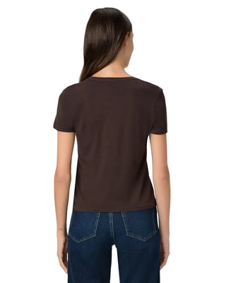 A woman viewed from the back wearing a dark brown short-sleeve crewneck t-shirt and blue jeans, set against a plain light gray studio background.