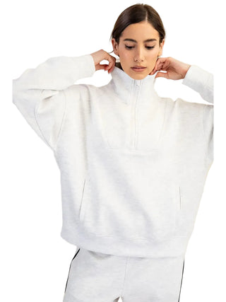 A woman wearing a light heather gray half-zip sweatshirt and matching sweatpants, posing against a solid beige background.