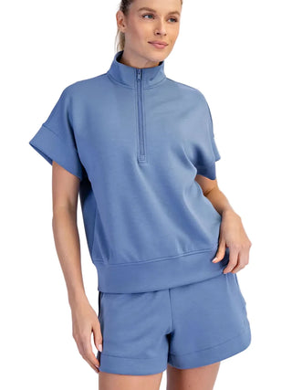 Woman wearing a blue short-sleeve top and shorts set on a light gray background