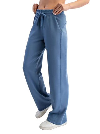 A person wearing wide-leg blue sweatpants with an elastic drawstring waist, shown from the torso down against a plain light background.
