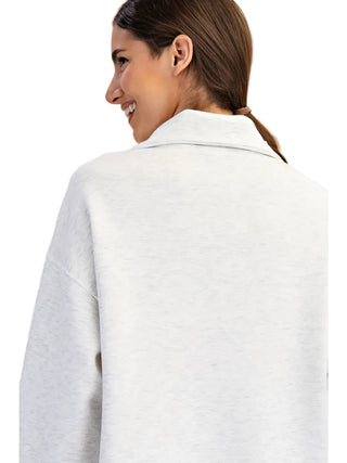 A woman shown from the back wearing an oversized light heather gray sweatshirt or pullover against a plain beige studio background.