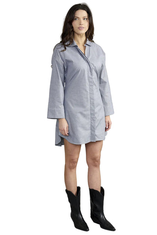 A woman modeling a light blue button-up shirt dress with three-quarter sleeves and black pointed-toe cowboy boots, photographed against a solid gray studio background.