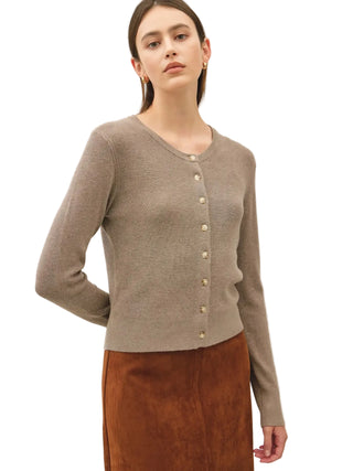 A woman wearing a taupe knit cardigan with gold buttons and a brown skirt, photographed against a plain light gray studio background.
