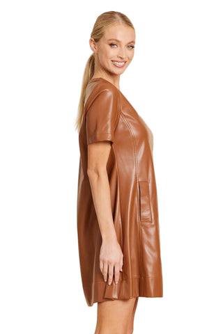 A woman modeling a short-sleeve brown faux-leather mini dress with a V-neckline, shown in profile against a solid beige studio background.