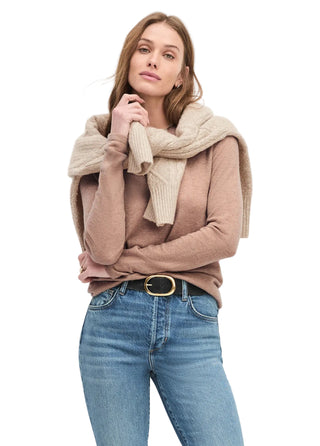 Woman wearing a beige sweater, scarf, and blue jeans against a white background