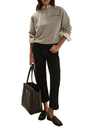 Person wearing a gray sweatshirt, black pants, and holding a black bag on a plain background