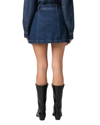 Rear view of a model wearing a blue denim mini skirt with a belt, a matching blue denim shirt, and black knee-high leather boots against a light gray studio background.