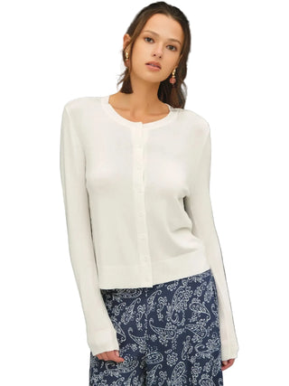 A woman modeling a white long-sleeve button-front cardigan sweater paired with navy blue paisley pants, set against a dark gray studio background.