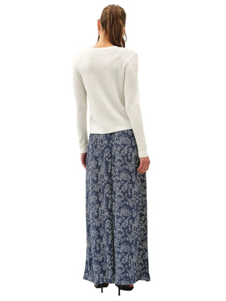 A woman shown from the back wearing a white long-sleeve top and a navy blue maxi skirt with a white floral pattern, standing against a plain white studio background.