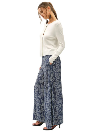 A woman modeling a white long-sleeve cardigan and blue-and-white patterned wide-leg pants against a plain off-white studio background.