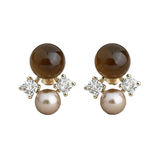 A pair of gold stud earrings featuring a large polished dark brown sphere, a smaller pale pink pearl, and two small clear cubic zirconia stones, displayed on a light gray textured fabric background.