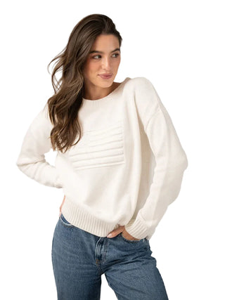 Woman wearing a white sweater and blue jeans against a plain background