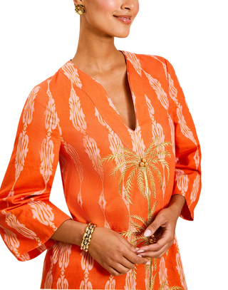 Orange dress with palm tree pattern worn by a model on a white background