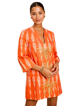 Woman wearing an orange dress with palm tree pattern on a white background
