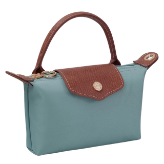 A small top-handle handbag in dusty blue with brown textured leather trim and a gold-tone snap-button closure, shown on a plain white background.